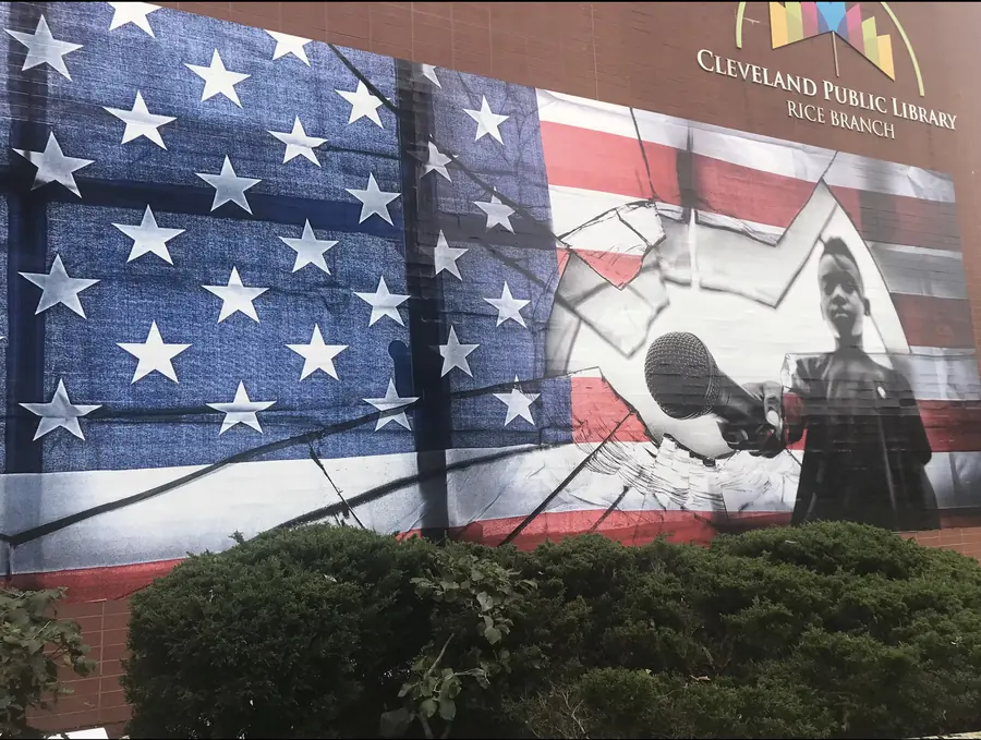 A mural of a cracked American flag with a hand holding a microphone, on the wall of the Cleveland Public Library Rice Branch.