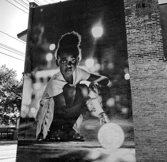 A mural of a young girl crouching against a brick wall, a bright orb of light glowing in her hand.