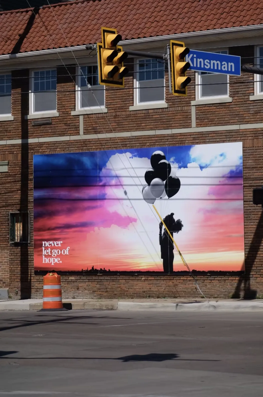A mural at Kinsman Road: a silhouetted figure holding a bunch of balloons against a pink and blue sunset over the Cleveland skyline, captioned ‘never let go of hope.’