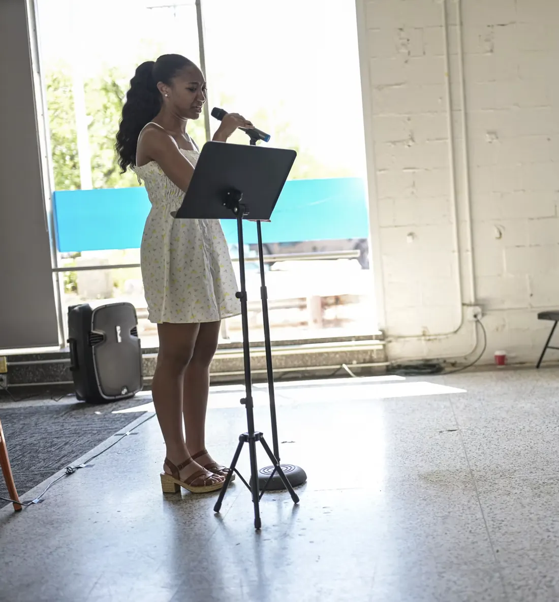 A young woman reads a poem from a music stand into a microphone.